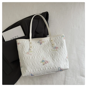 Gros plan du sac cabas matelassé blanc avec broderies papillons colorées et texture à motif E