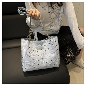 Detail of light blue tote bag with pleated fabric, black bows and metal chain strap