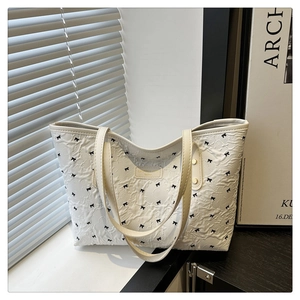 Detail der weißen Plissee-Tasche mit schwarzen Schleifen-Stickereien und Leder-Tragegriff