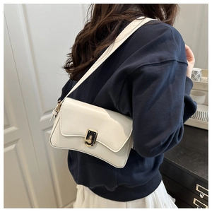 Detail view of a white minimalist shoulder bag with unique golden rotary lock on the flap
