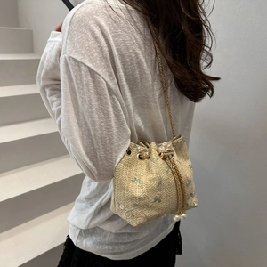 Beige woven bucket bag with floral embroidery and gold chain strap shown on model