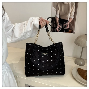 Detail of black quilted tote bag featuring white bow jacquard and gold metal strap rings