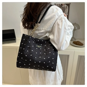 Detailed view of black pleated tote bag with bow embroidery and gold chain details