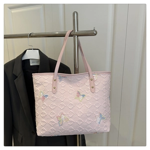 Gros plan du sac cabas rose matelassé avec broderies papillon colorées et finitions soignées