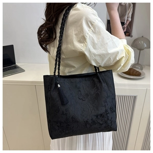 Detail of black butterfly textured tote bag with woven straps and silk tassel pendant
