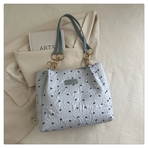 Detail of light blue quilted tote bag featuring black bow prints and gold chain strap
