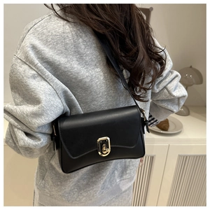 Close-up of a minimalist black leather crossbody bag with a gold twist-lock on a model