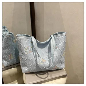 Détail du sac cabas bleu clair avec texture matelassée et broderie papillon élégante