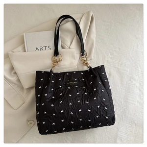 Detail of black quilted tote bag with white bow patterns and gold chain hardware