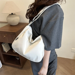 Minimalist white canvas crossbody crescent bag worn by model in cozy interior setting