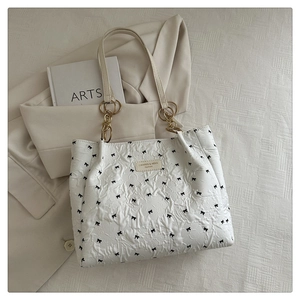 Detail of white quilted tote bag with floral texture and black bow embroidery