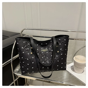 Detail einer schwarzen Stepptasche mit weißen Schleifenmustern und edlem Namensschild