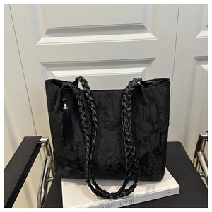 Detail of black tote bag featuring butterfly embroidery and braided straps with fringe tassel