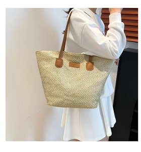 Détail du sac cabas en paille beige avec anses en cuir marron et écusson en cuir mode