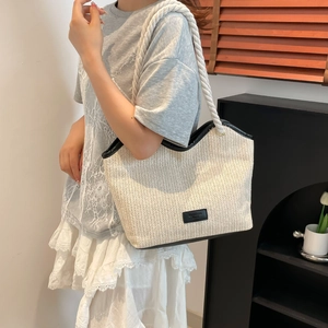 Detail of white straw tote bag with rope handles and black leather fashion logo patch