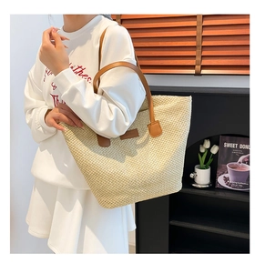 Détail d'un sac cabas en paille tressée avec poignées en cuir marron et fini beige