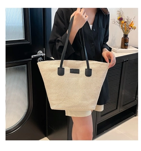Détail d'un grand sac cabas tressé beige avec anses noires et étiquette de mode en cuir
