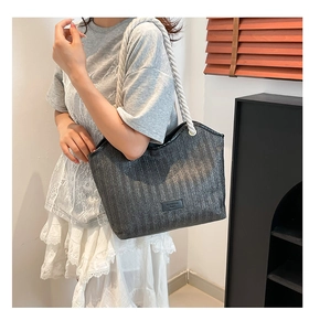 Detail of black woven tote bag featuring white rope straps and textured herringbone pattern