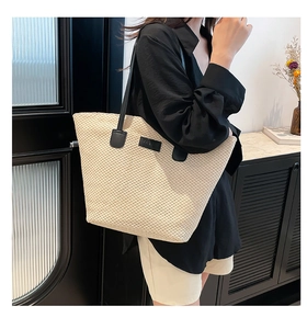 Détail d'un cabas tressé beige porté à l'épaule avec des poignées en cuir noir chic