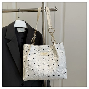 Detail of white tote bag with black bow patterns and elegant gold chain handles