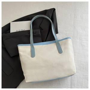 Detail of canvas tote bag featuring light blue leather trim and straps on white fabric