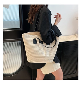 Détail d'un grand sac cabas en paille tissée avec anses noires porté à l'épaule par un mannequin