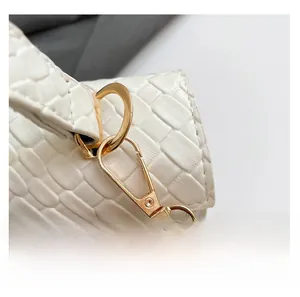 Detail of gold metal hook and woven texture on a white leather shoulder bag strap