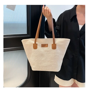Détail d'un sac seau tissé beige avec anses marron et patch en cuir décoratif