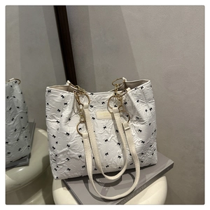 Detail of white textured tote bag with black bow print and golden chain handle