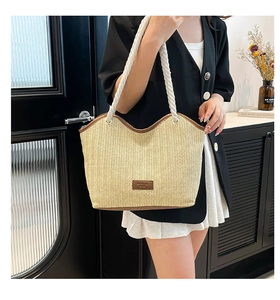 Detail of woven straw tote bag featuring brown leather patch and white rope strap handle