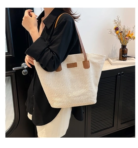 Gros plan du sac seau tissé beige avec bandoulière en cuir marron et détail de patch