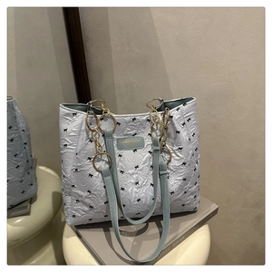 Detail of light blue tote bag with black bow print and gold chain strap on a stool