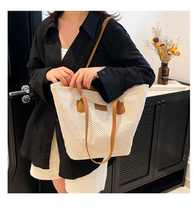 Détail d'un sac cabas tissé crème avec anses en cuir marron et étiquette logo épurée