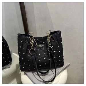 Detail of black quilted tote bag with white bow pattern and golden chain handle strap