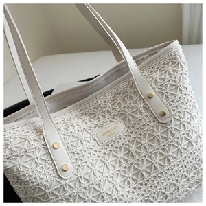 Detailed close-up of straw woven tote with leather logo tag and gold rivet accents