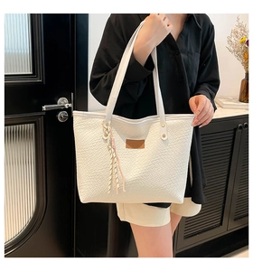 Détail macro du sac cabas blanc tissé avec étiquette en cuir et pompon rayé chic