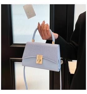 Close-up of light blue handbag showing woven texture flap and golden twist-lock buckle