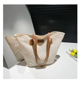 Détail du sac cabas en paille tressée avec poignées en cuir marron et écusson