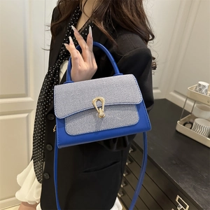 Close-up of a royal blue leather bag featuring a gold horseshoe metal buckle and denim texture