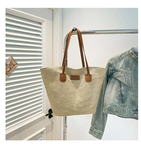 Détail d'un grand sac cabas en paille avec lanières en cuir marron et écusson mode