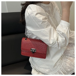 Gros plan sur un sac à bandoulière rouge tressé avec fermoir géométrique et chaîne en métal
