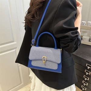 Detail of royal blue textured leather handbag with gold horseshoe buckle and striped fabric