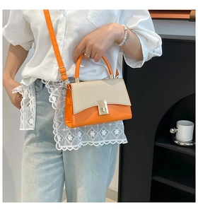 Detail of a bright orange crossbody bag with a beige woven flap and gold metal lock