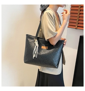 Détail du sac cabas en cuir noir tressé avec pompon et motif à carreaux texturé