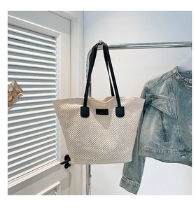 Détail du sac cabas en paille blanche avec anses en cuir noir et écusson central