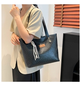 Détail du sac cabas tressé noir avec étiquette en cuir et pompon décoratif élégant