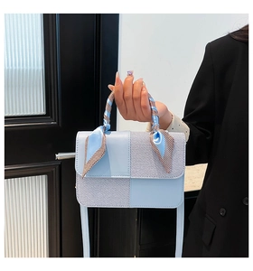 Close-up of light blue fashion handbag with textured patchwork and decorative silk scarf
