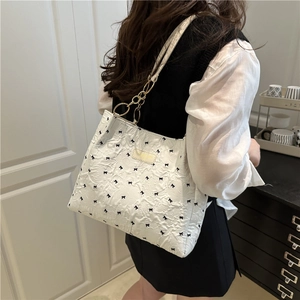 White textured tote bag with black bow prints and gold metal rings shown on a model