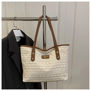Close-up of white lace woven tote bag featuring brand logo and brown leather straps