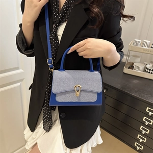 Detail of royal blue textured leather handbag with gold horseshoe buckle on model